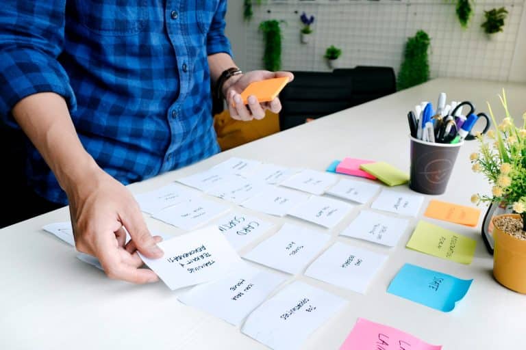 A man in a blue flannel lays out sticky notes on a white desk, each with some text written.